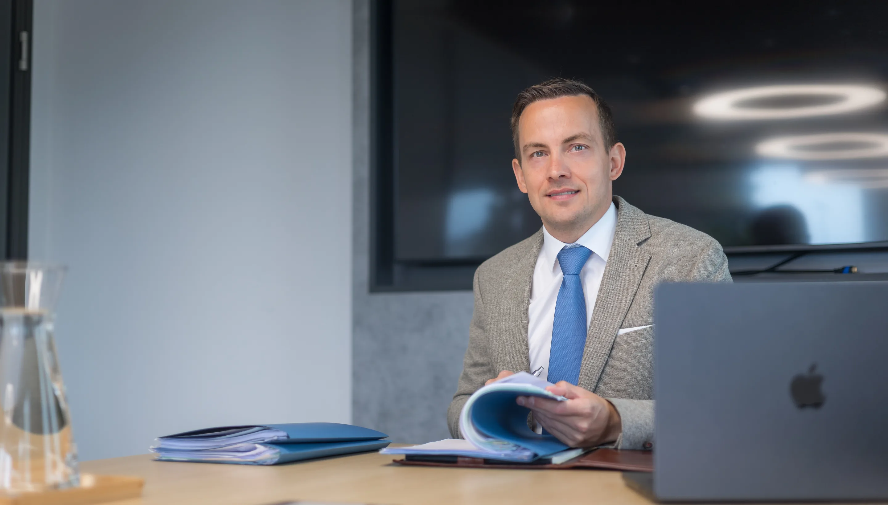 Dr. Daniel Holzinger blättert hinter dem Laptop in einer Mappe