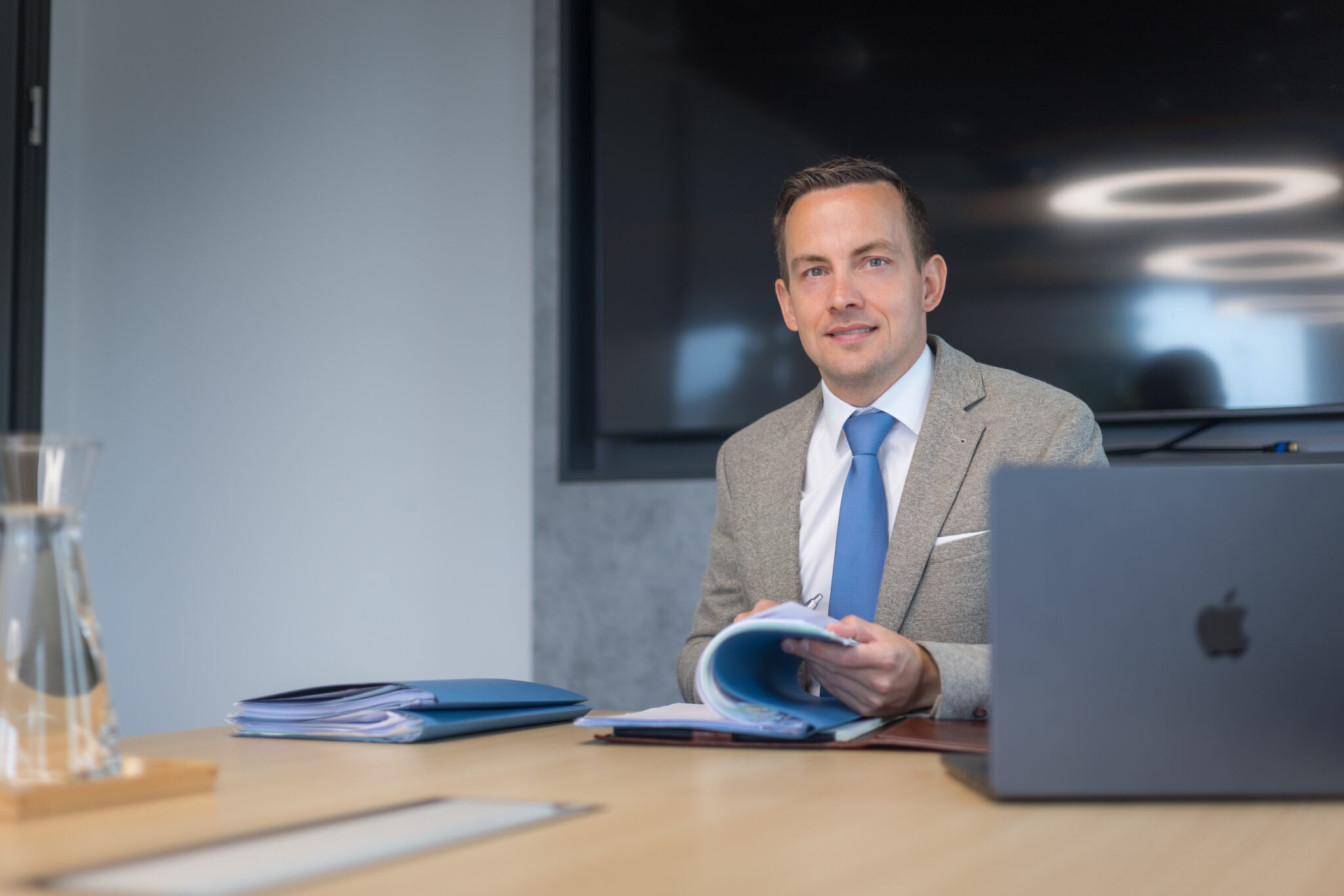 Dr. Daniel Holzinger blättert lächelnd in einer blauen Mappe am Besprechungstisch
